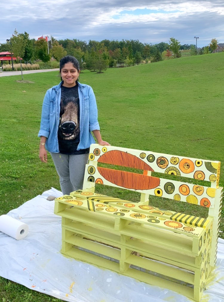Person standing next to a colorful bench made from painted wooden crates in a park.